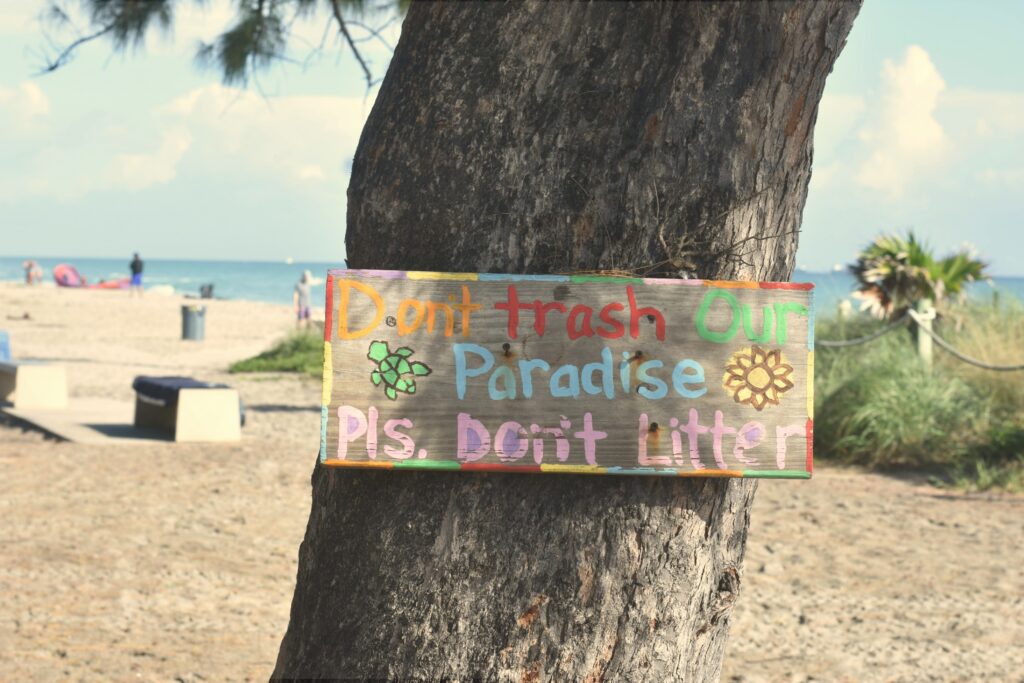 beach with sign posted that says "Don't trash our paradise. Please don't litter" to promote travel with purpose